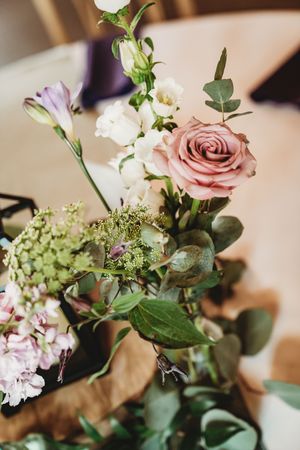 Elegant floral arrangement featuring a pink rose, white lisianthus, eucalyptus, and soft blooms in a rustic table centerpiece.