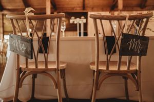 Rustic wooden wedding chairs with elegant Mr. and Mrs. chalkboard signs at a reception venue.