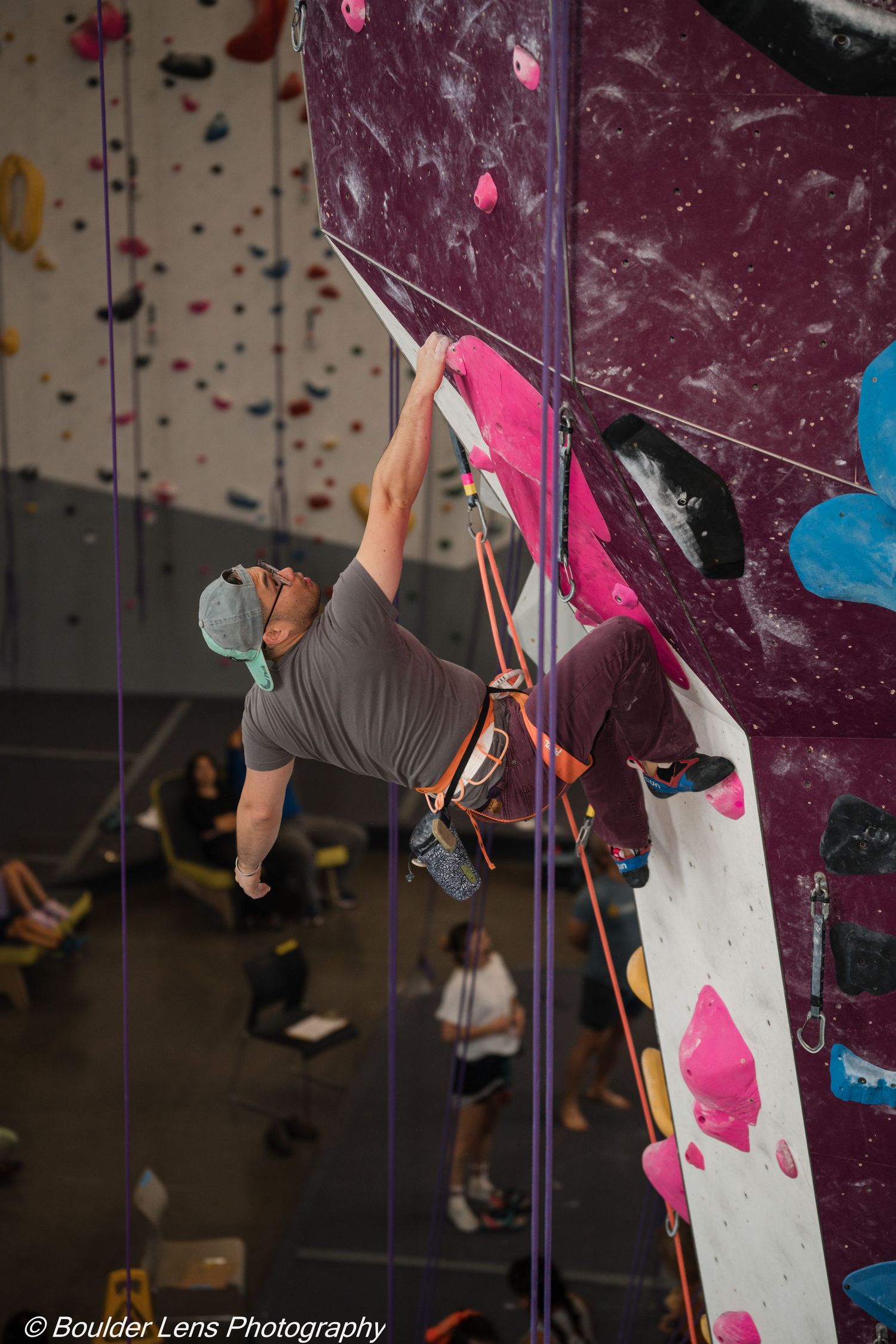 Rock climber scaling an indoor climbing wall with colorful holds at a climbing gym.