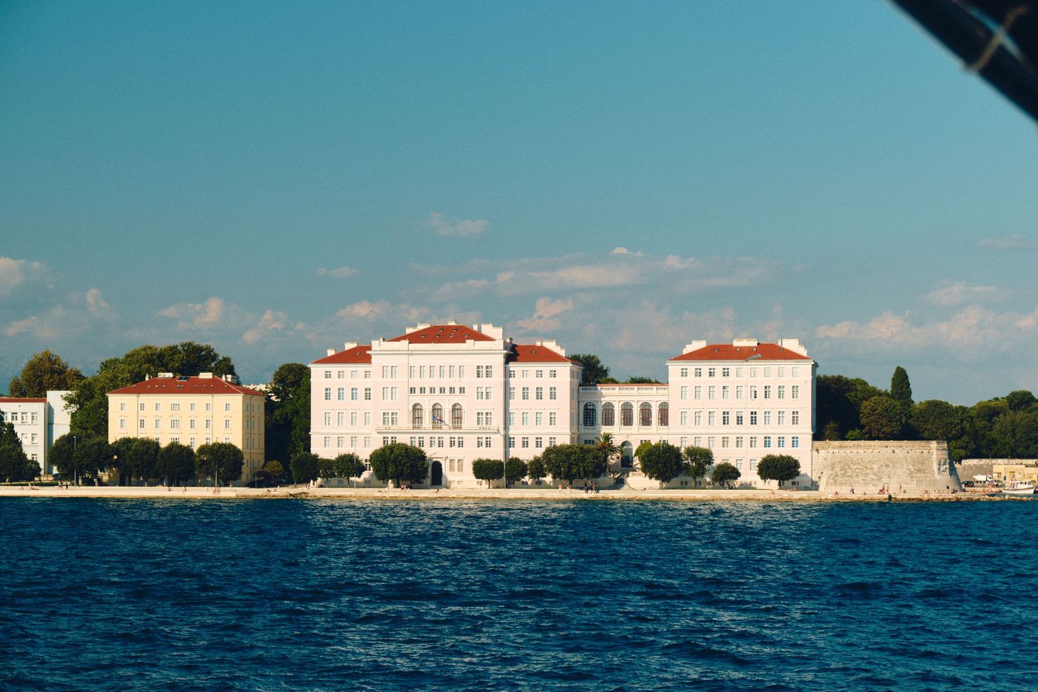 Grand white historic buildings along the Mediterranean coastline with red-tiled roofs.