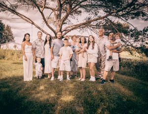 Large family group portrait under a sprawling tree in casual summer attire.