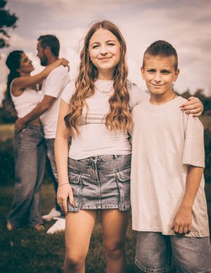 Family portrait of children posing together outdoors with adults in background.