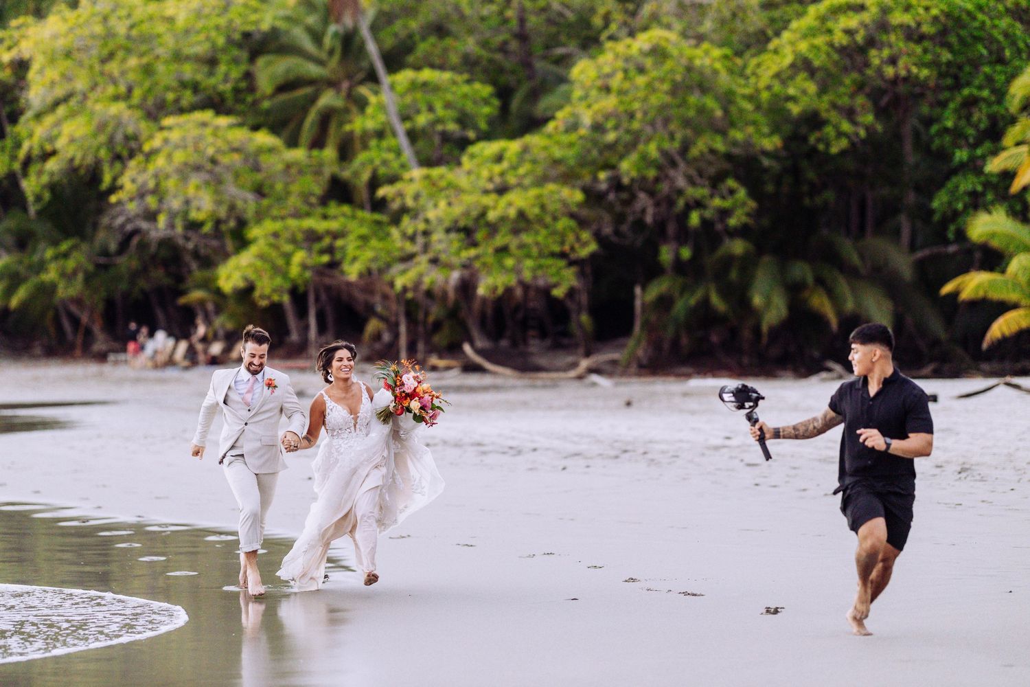 Wedding photographer capturing couple running on tropical beach with palm trees.
