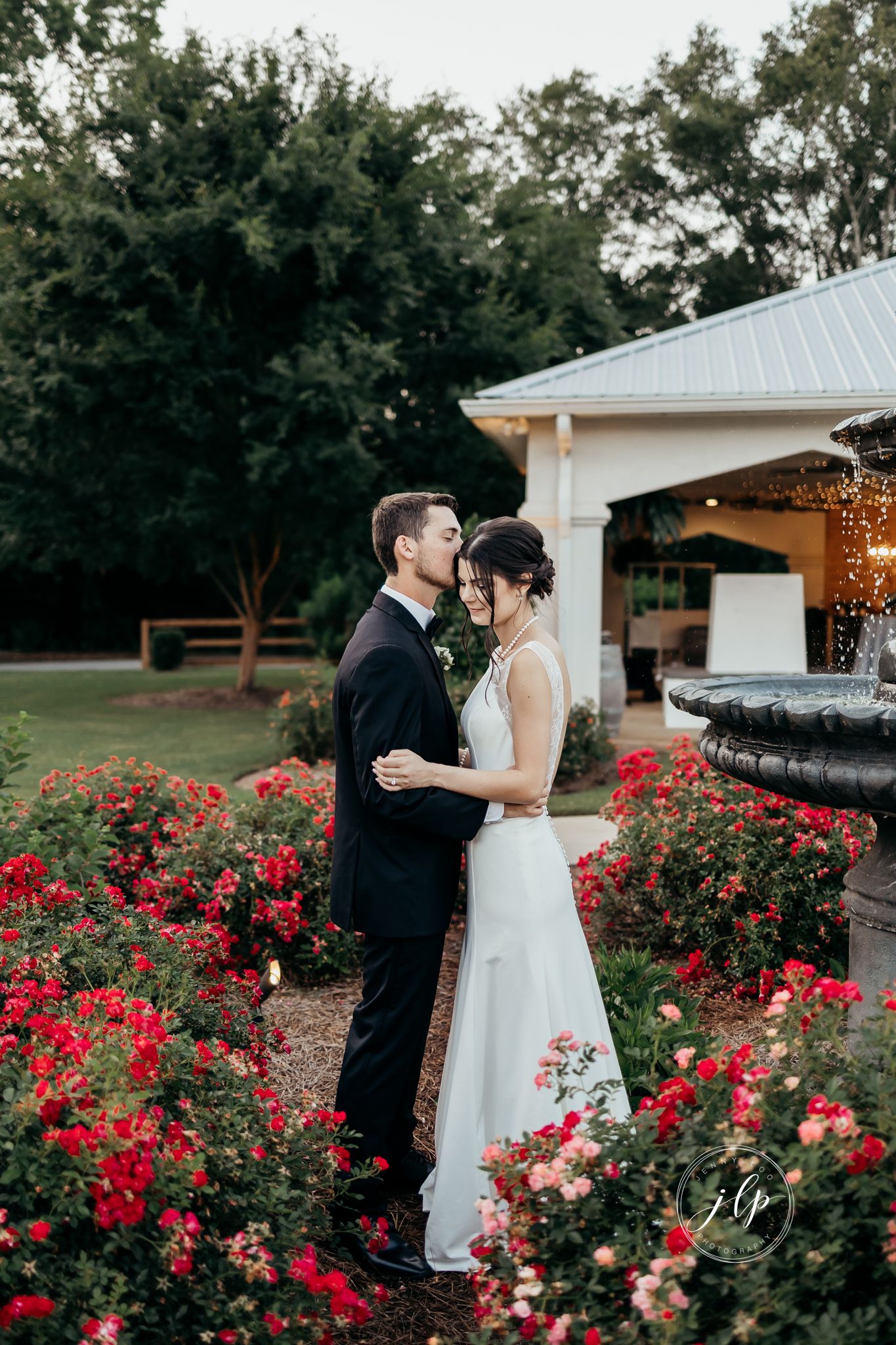 A romantic moment captured between a couple among blooming red rose bushes.