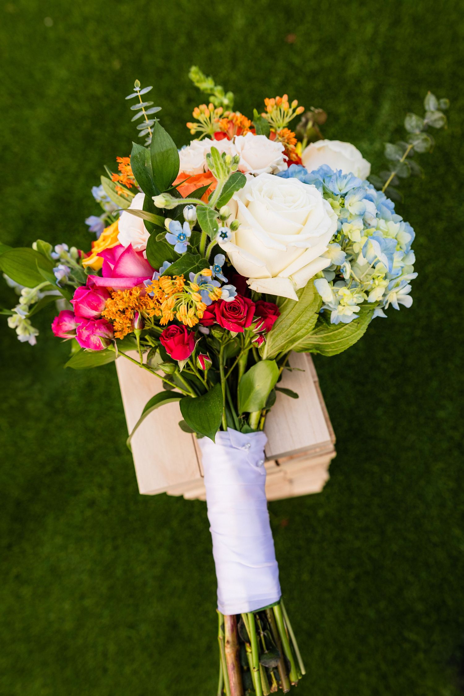 Colorful bridal bouquet with roses, hydrangeas and greenery wrapped in white ribbon.