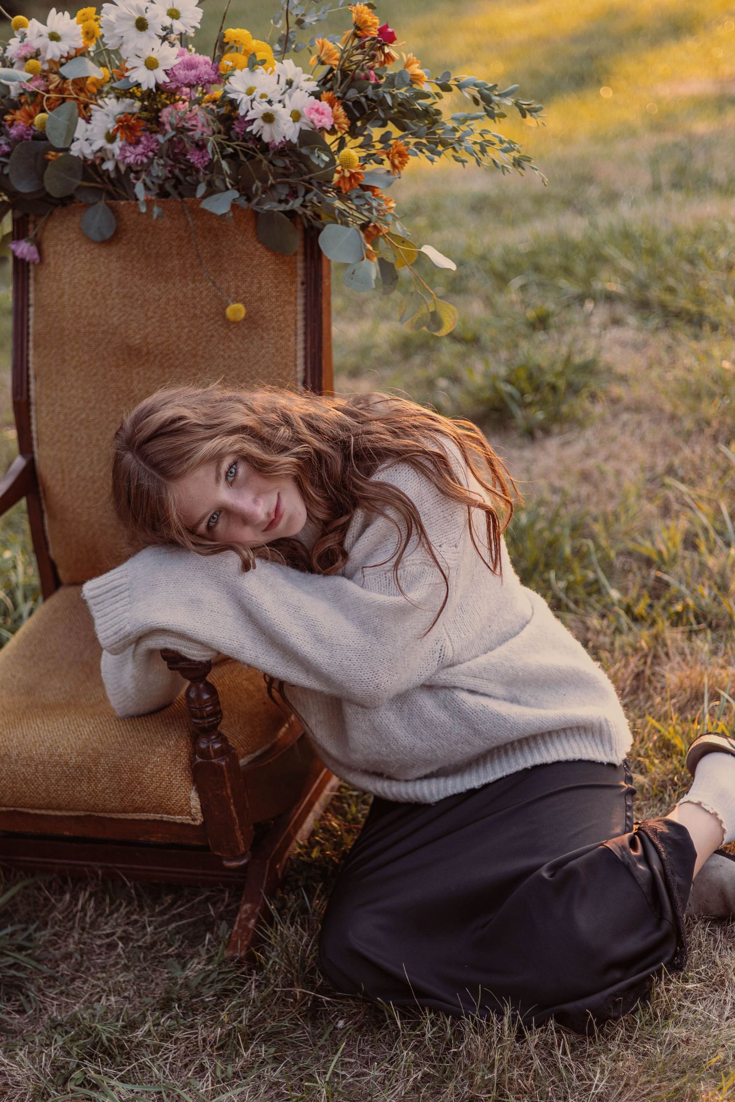 Romantic autumn portrait with floral arrangement and cream sweater against golden sunlight.