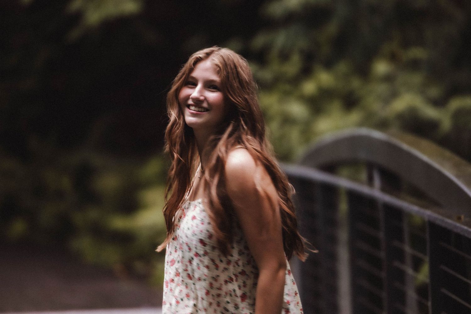 A summer portrait showing a flowing floral dress against a natural wooded background with a bridge.