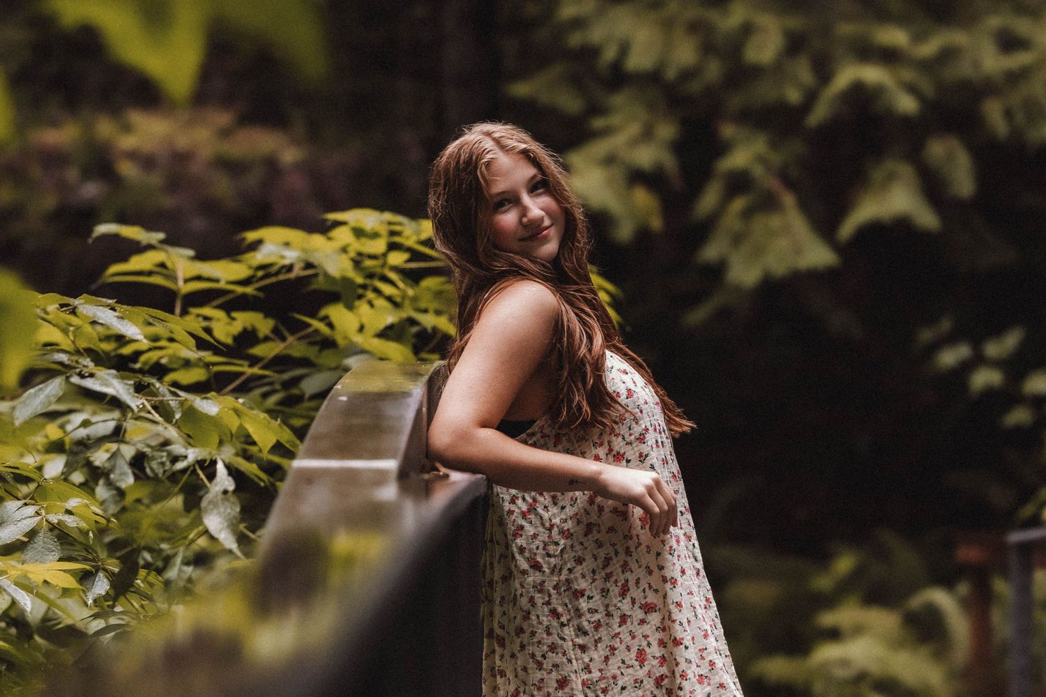 Portrait in a floral sundress surrounded by lush green foliage and natural lighting.