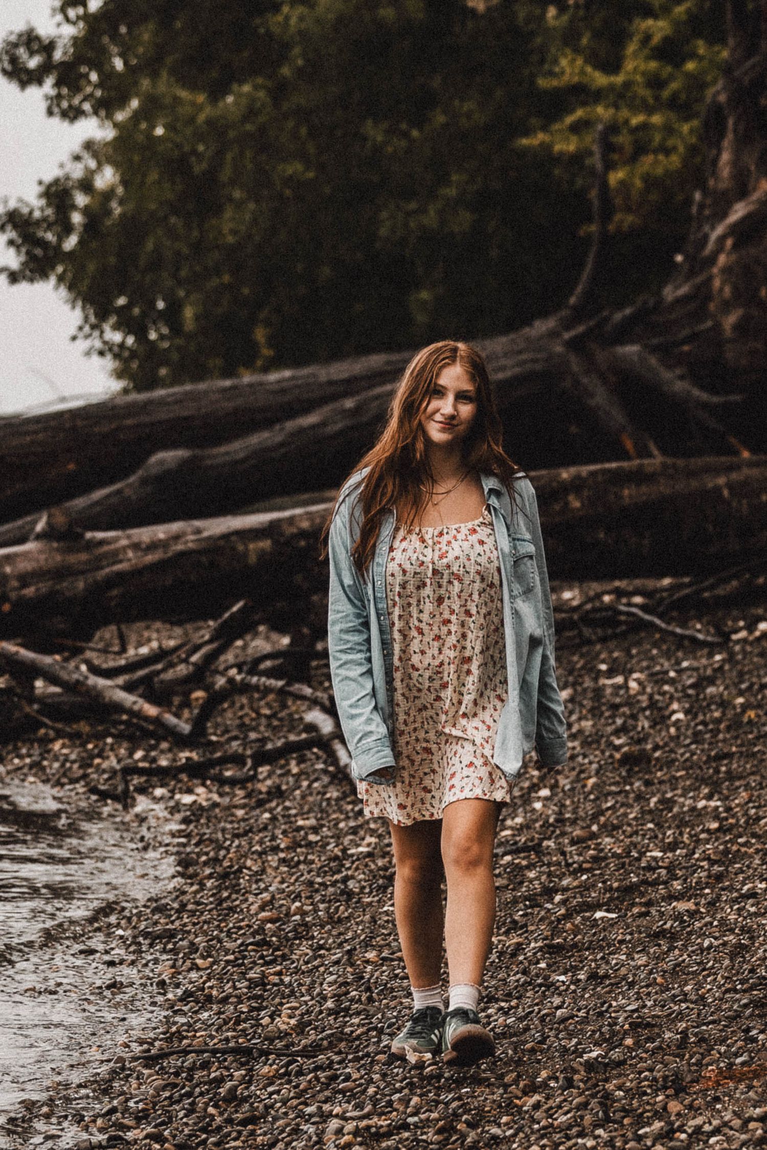 Casual portrait by the shoreline wearing a floral dress and denim jacket.