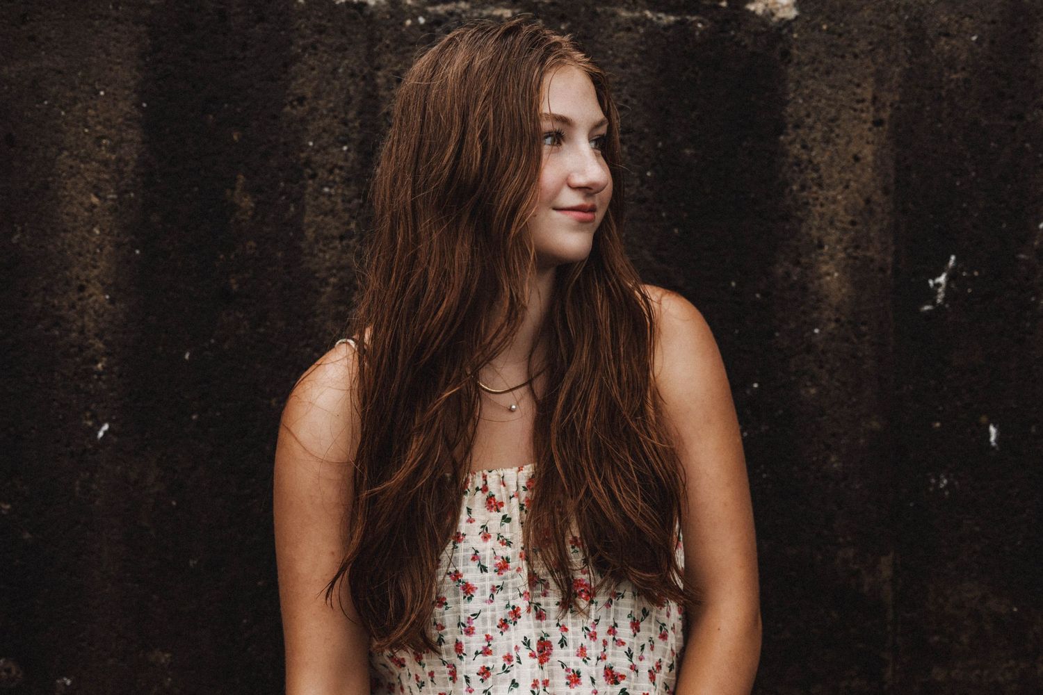 Artistic portrait against a dark textured wall wearing a floral summer dress.