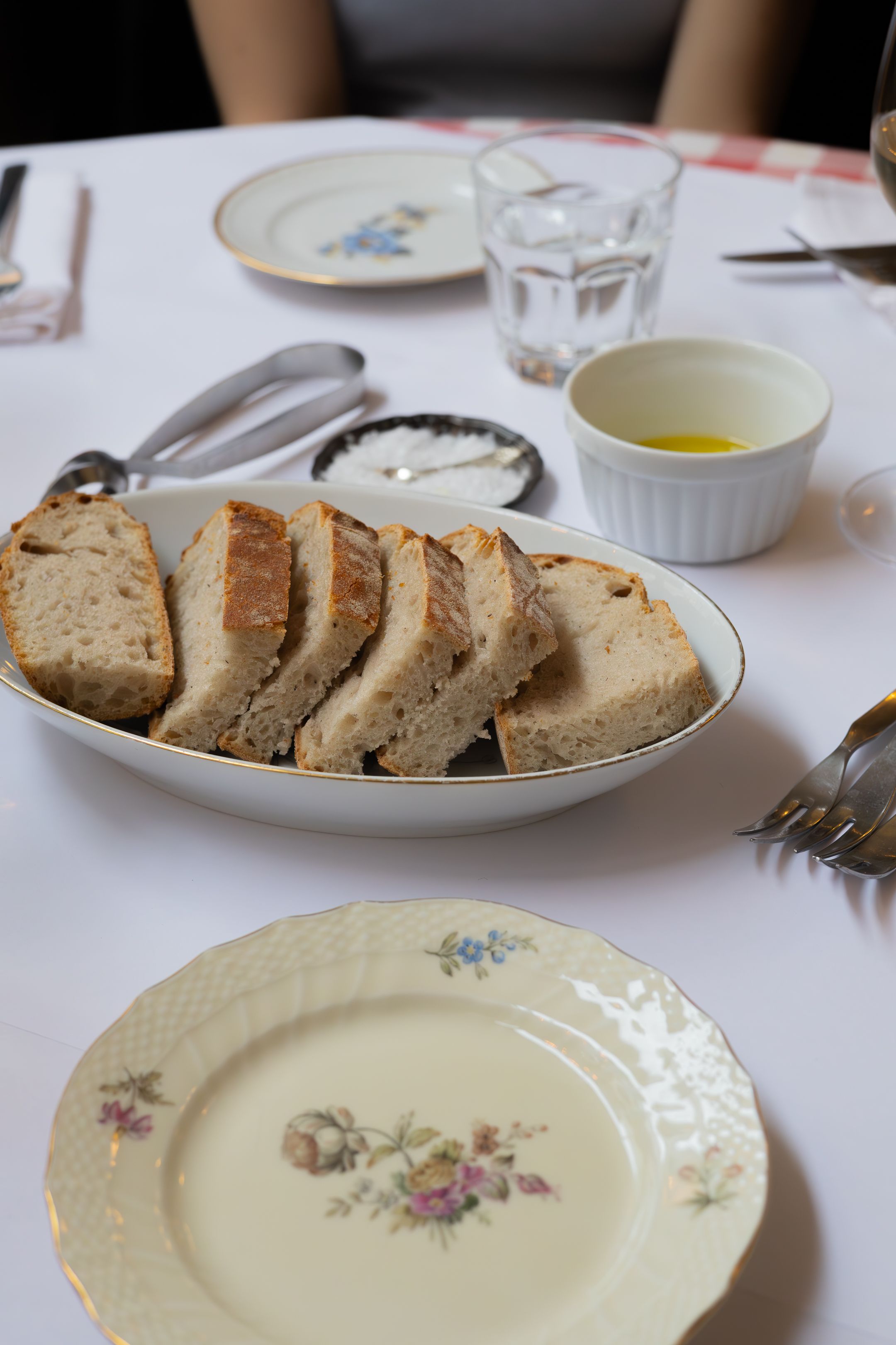 Sliced rustic bread on a floral plate with butter and oil accompaniments.