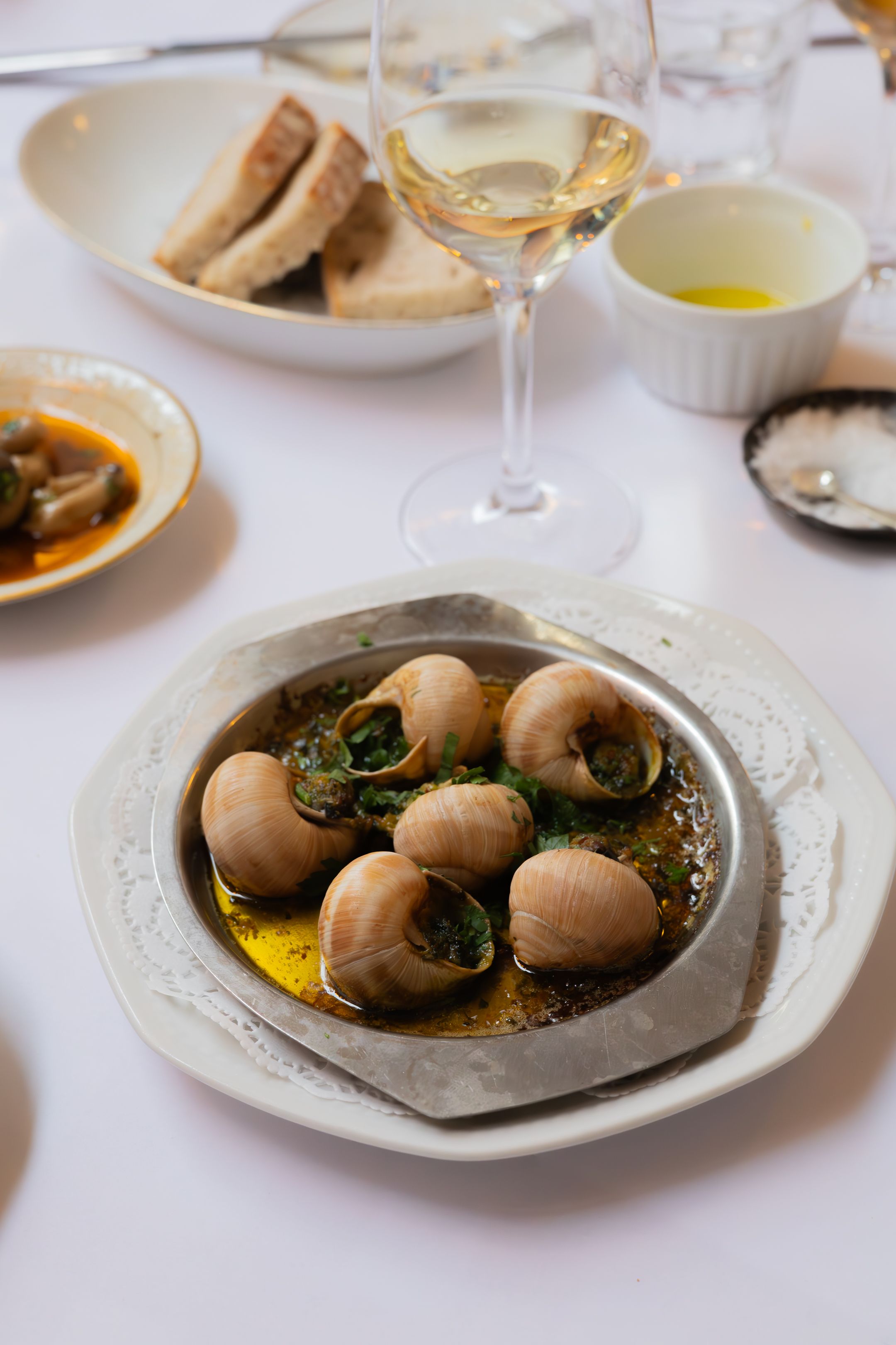 Escargot in garlic butter sauce served on an elegant white plate with wine and bread.