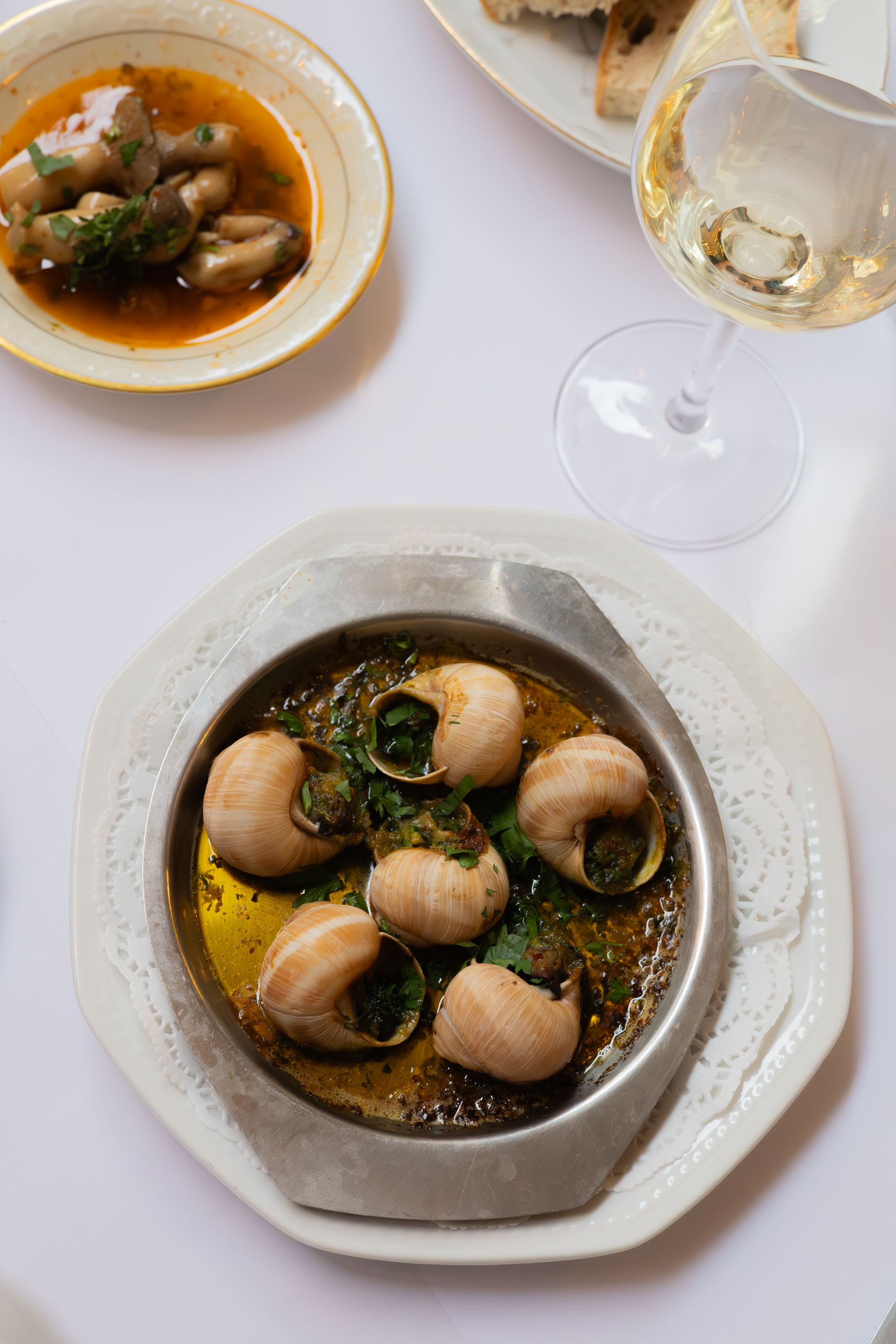 Escargot in herb butter sauce on a decorative plate with wine glass in background.