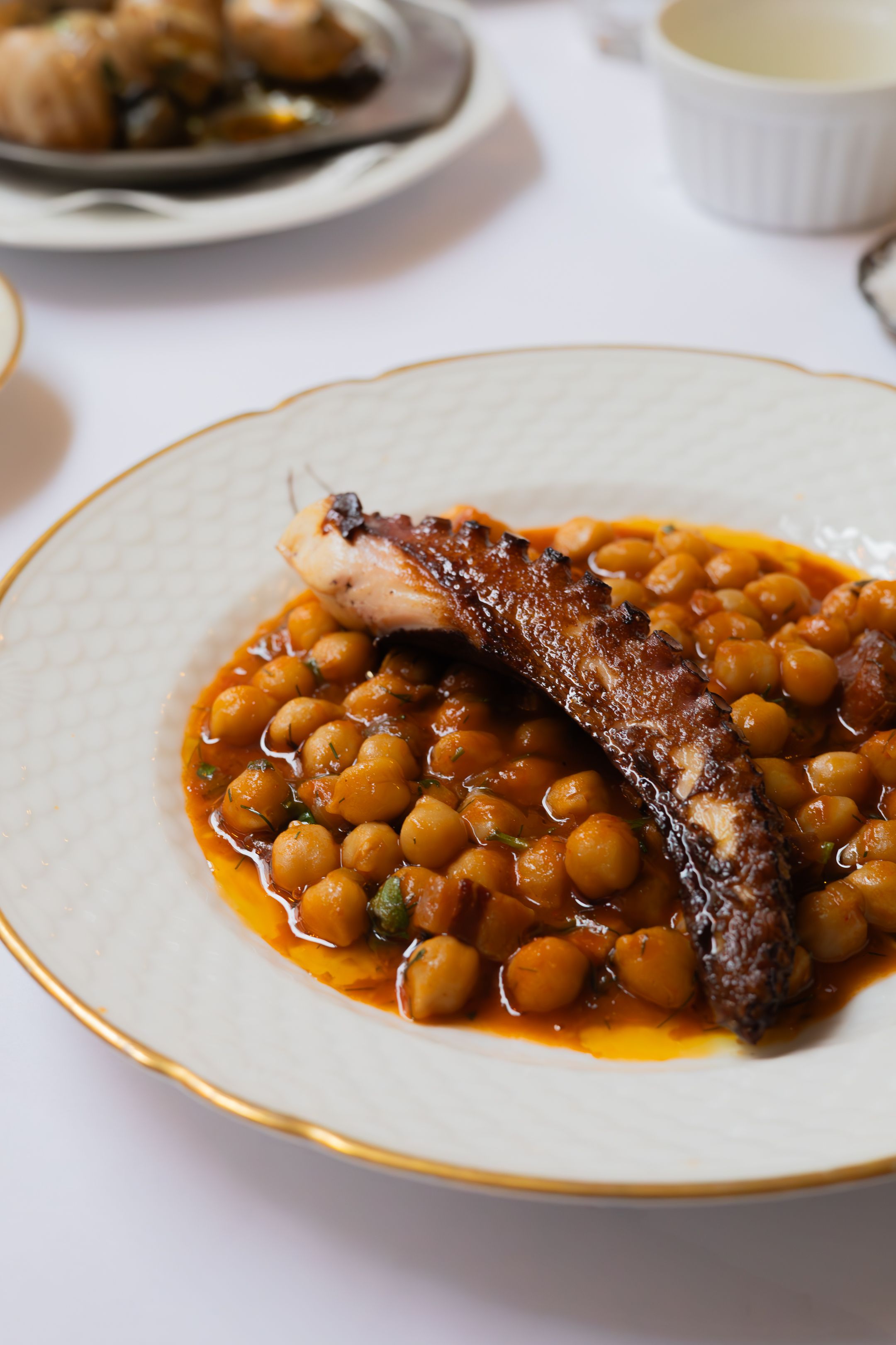 Braised meat served with chickpeas in a rich orange sauce on a white plate.