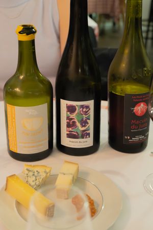 Selection of artisanal cheeses displayed with three natural wine bottles on a white plate.