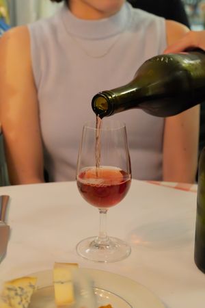 Red wine being poured into a stemmed wine glass with cheese plate in the foreground.