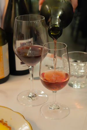 Two glasses of red wine being filled from a dark bottle on a white tablecloth.