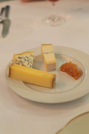 Cheese plate featuring blue cheese, hard yellow cheese, and fruit preserve on white porcelain.