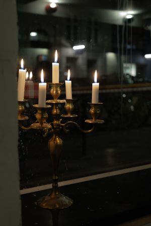 Antique brass candlestick holder with burning white candles against dark background.