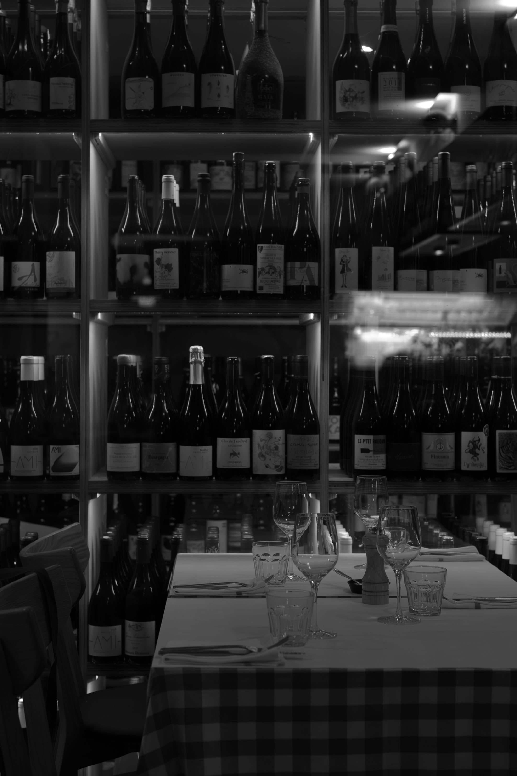 Black and white image of wine bottles lined on shelves above a checkered tablecloth.
