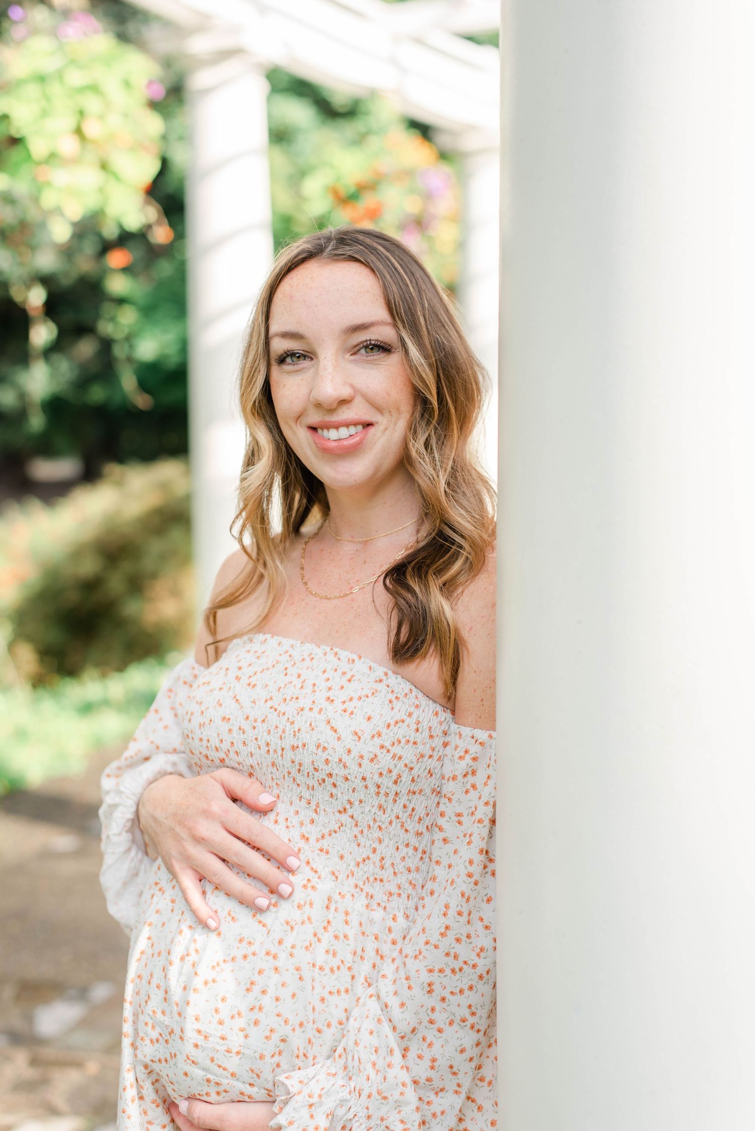 A stunning maternity portrait with a floral dress against white columns outdoors.