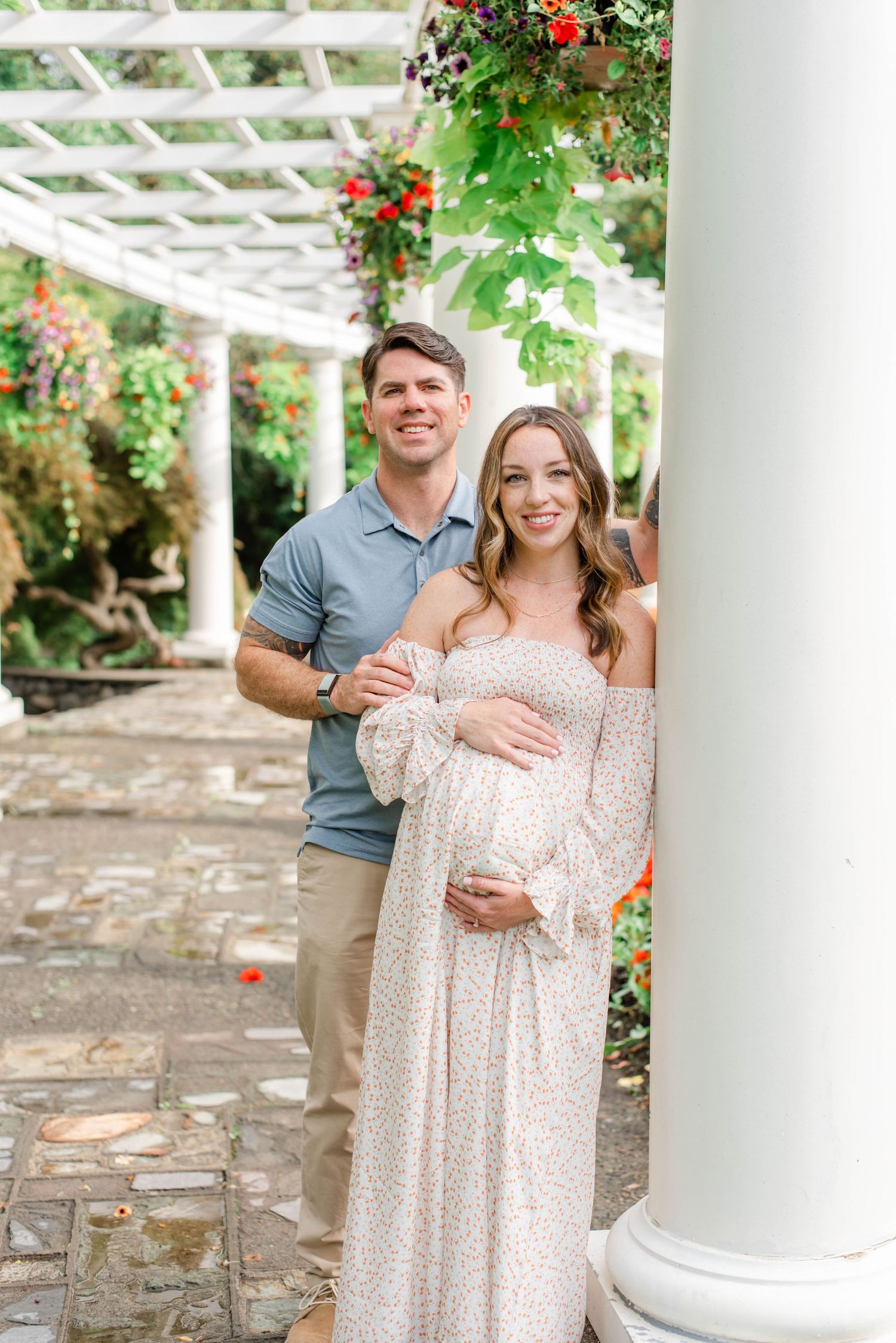 A romantic maternity photoshoot with couple in garden setting with white columns.