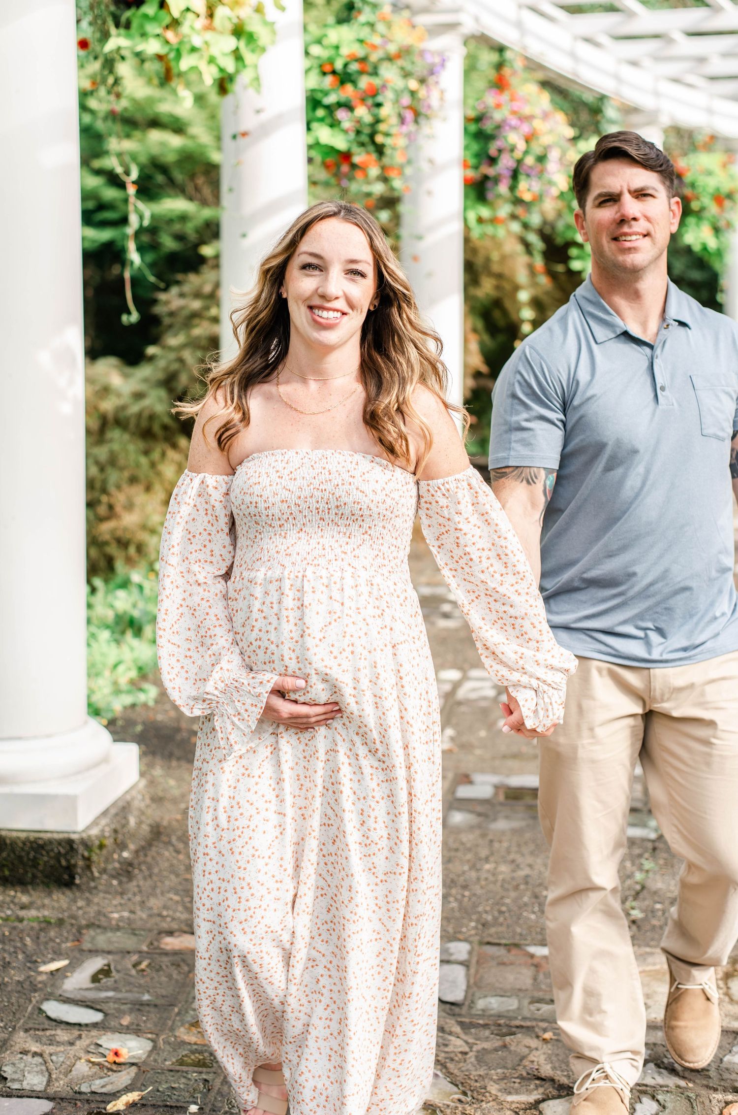 Outdoor maternity photos showing couple in casual attire under white pergola.