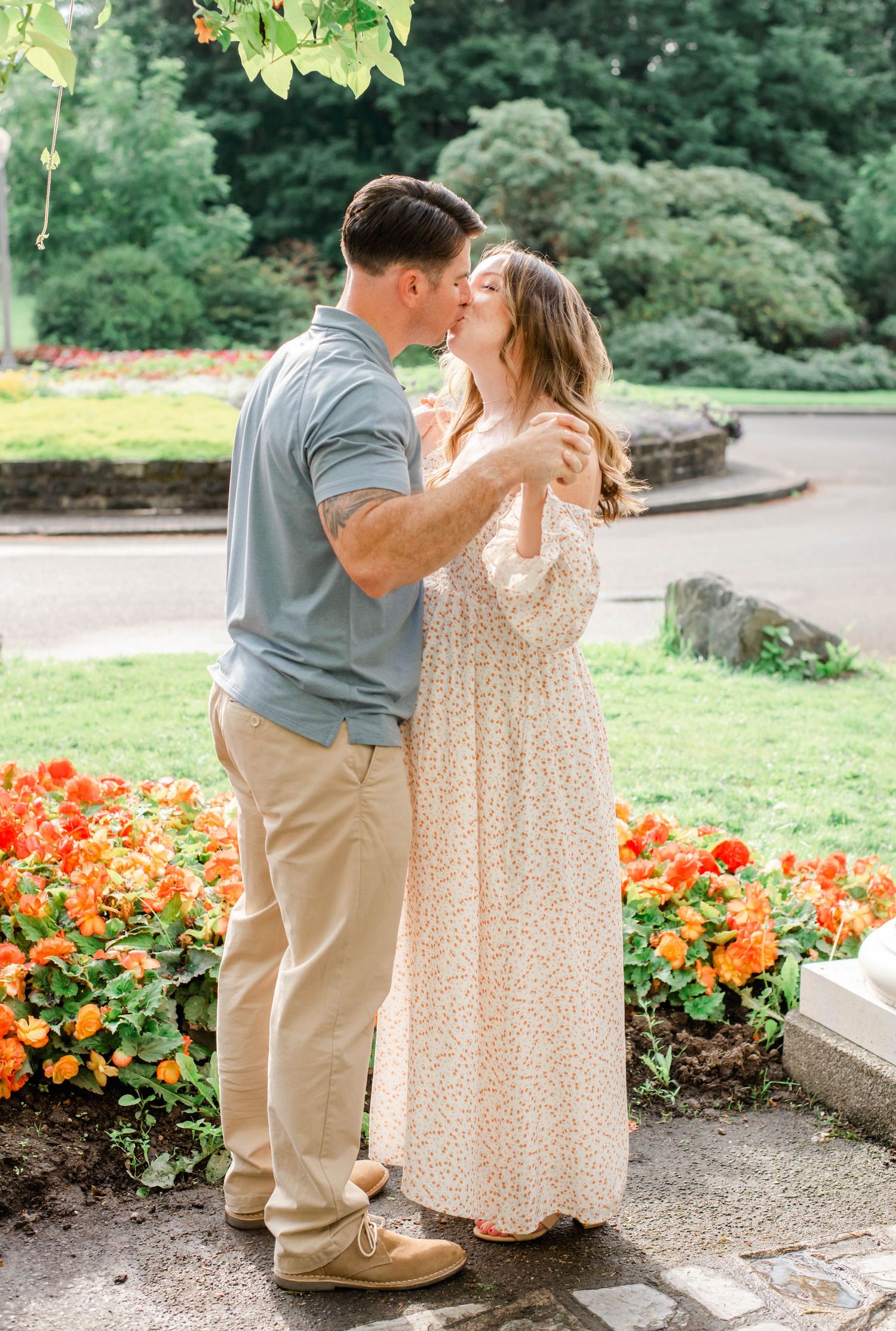 A romantic moment captured in a garden setting with orange flowers and greenery in the background.