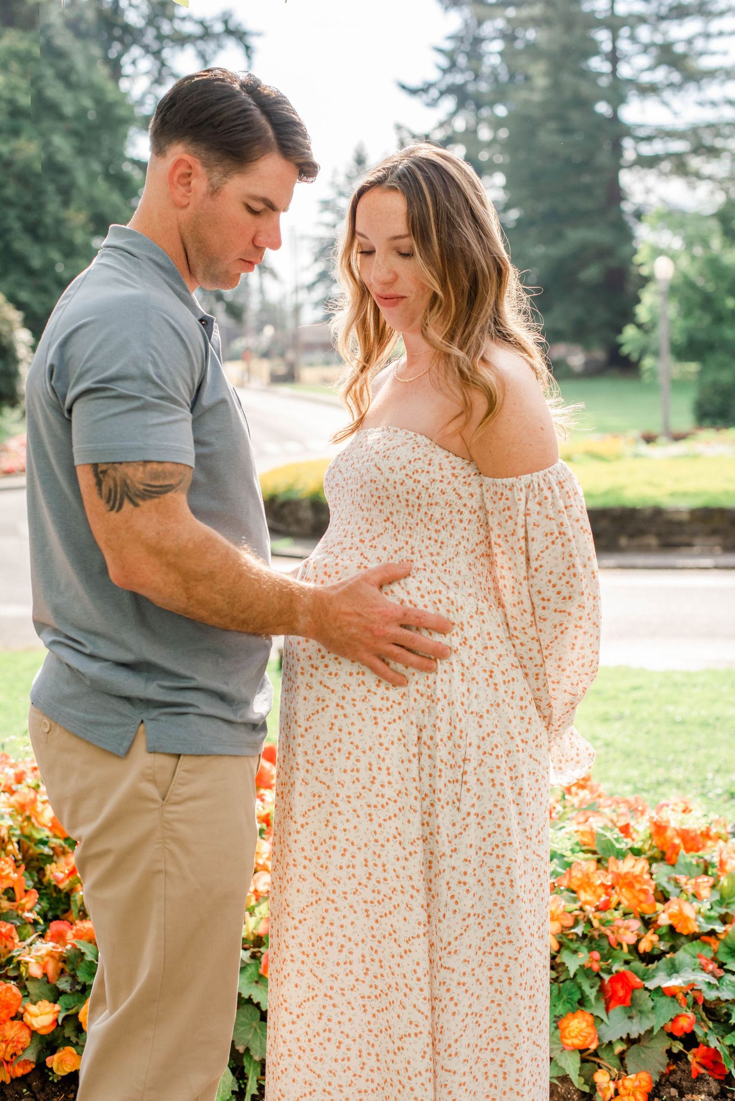 Couple sharing a tender moment in a garden with bright orange flowers and evergreen trees.
