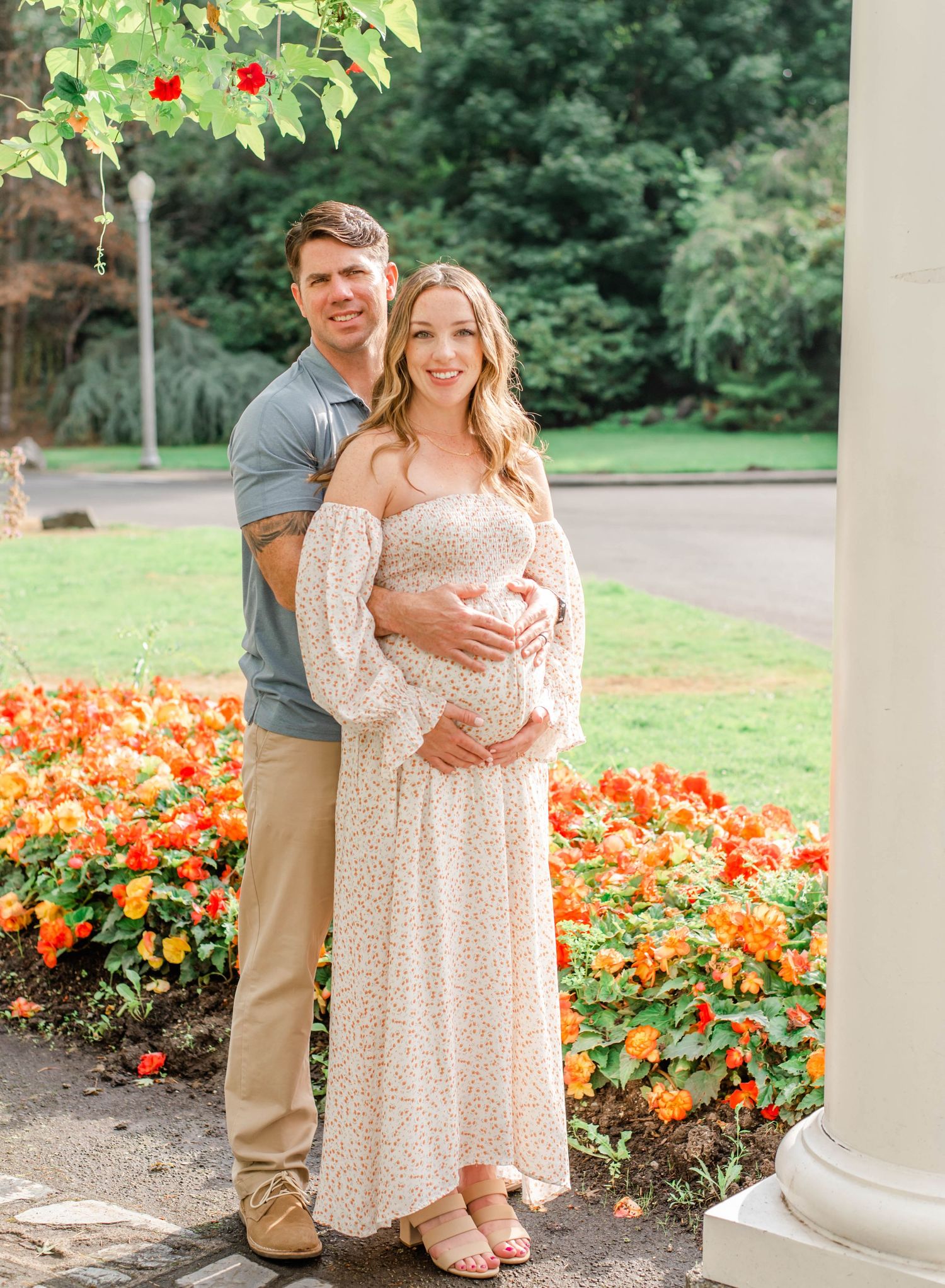 Garden photoshoot featuring a couple by a white column surrounded by vibrant orange flowers.