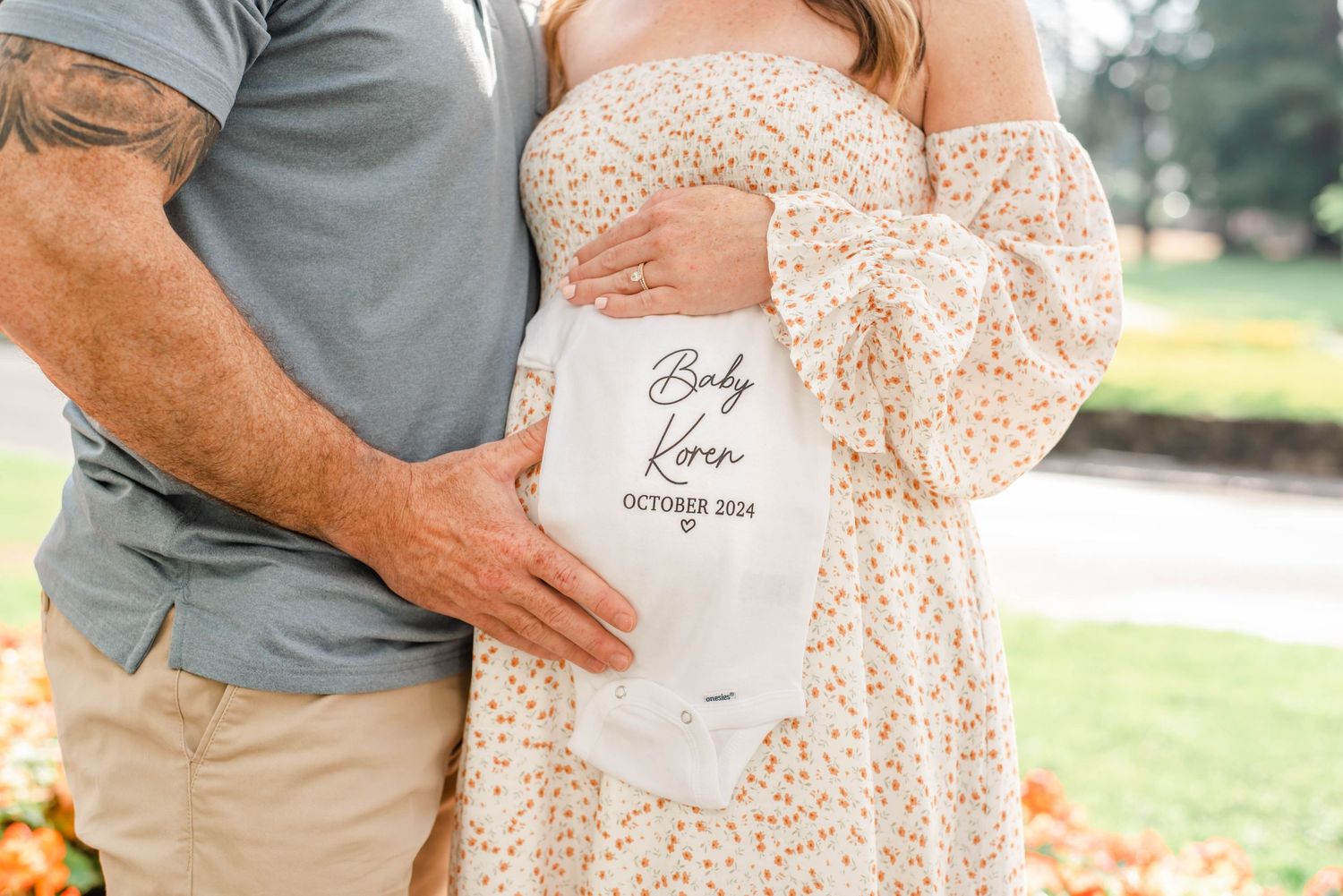 Close-up of hands holding a white baby announcement sign against a floral dress.