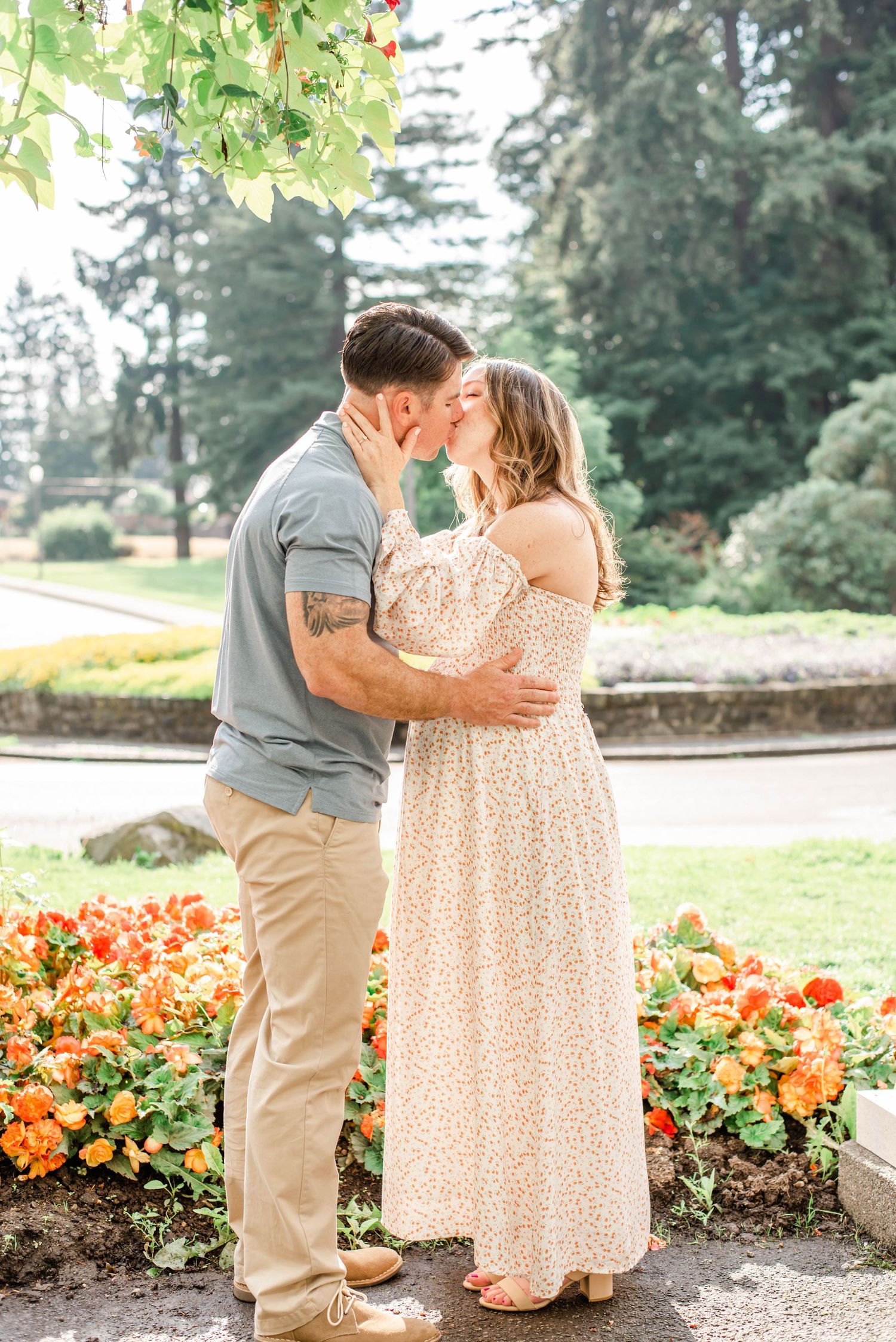 Romantic moment captured in garden setting with orange flowers and evergreen trees in background.