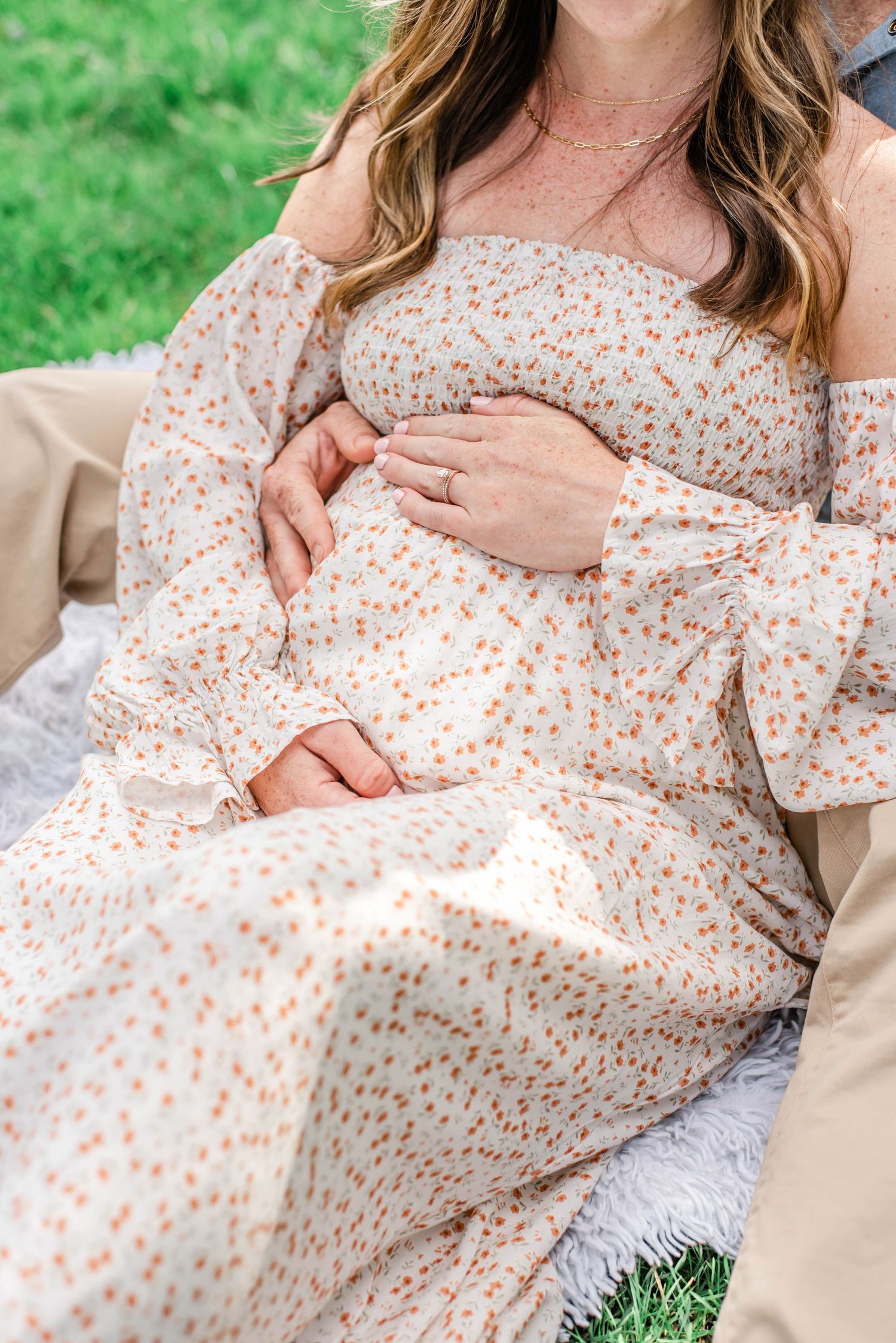 Close-up of floral maternity dress detail with hands resting on baby bump.