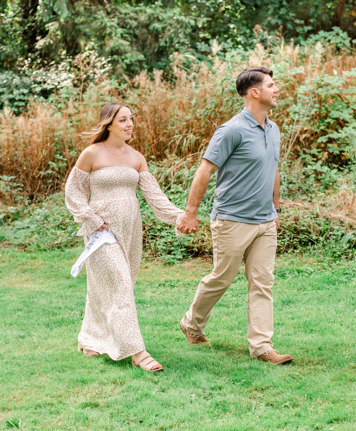 Couple walking hand in hand through garden path with tall grasses in background.