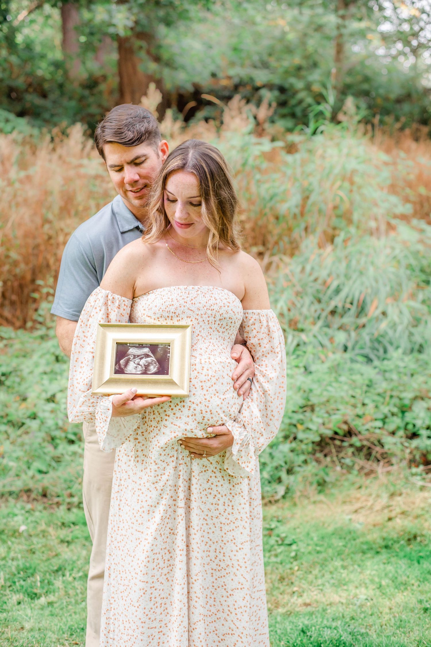 Couple holding ultrasound photo frame in garden setting during maternity photoshoot.