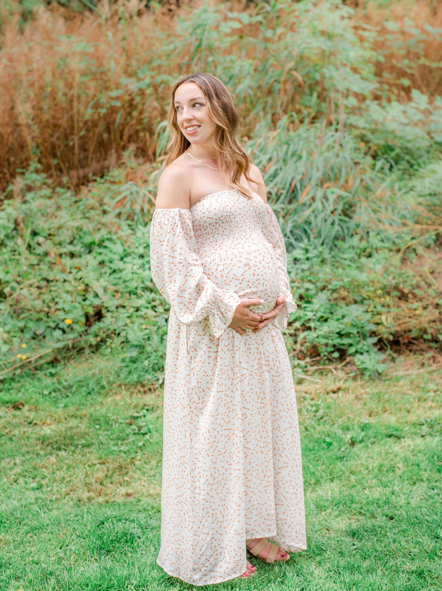 Woman in flowing white dress poses gracefully against a backdrop of greenery.