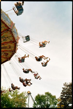 People enjoying a thrilling ride on a spinning wave swinger carousel at an amusement park against a blue sky.