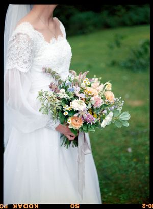 A beautiful wedding bouquet with pastel flowers and greenery against a white lace dress.