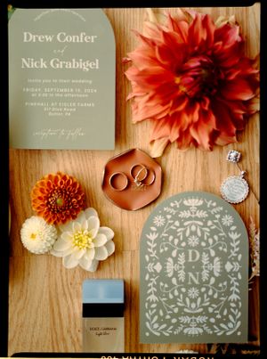 Wedding invitation and floral details with rings on wooden surface.