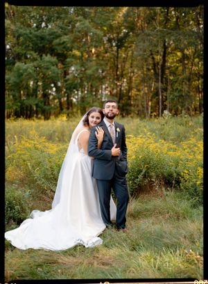 Newlyweds pose together in field of yellow wildflowers and autumn trees.