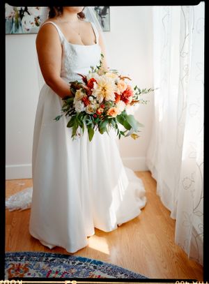 Person in white wedding dress holding a vibrant coral and peach floral bouquet.