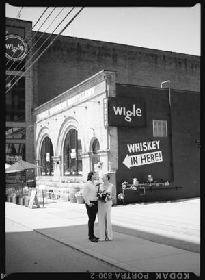 Vintage black and white photograph of a storefront with arched architecture and a 'Whiskey in here!' sign.