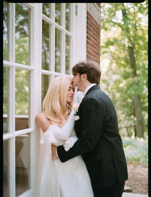 A couple in wedding attire share a tender moment by a window.