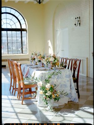 An elegant wedding reception table with floral centerpieces bathed in natural light from arched windows.