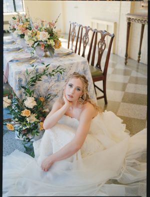 A bride in white sits by an elegantly decorated wedding reception table.