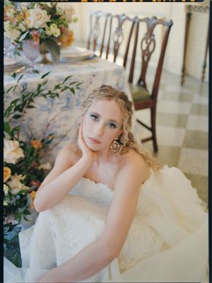 A bride in a strapless gown poses beside floral arrangements at a reception table.