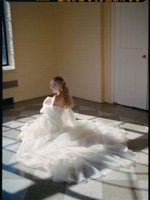 A bride in a flowing white dress sits gracefully on a sunlit floor, creating dramatic shadows and light patterns.
