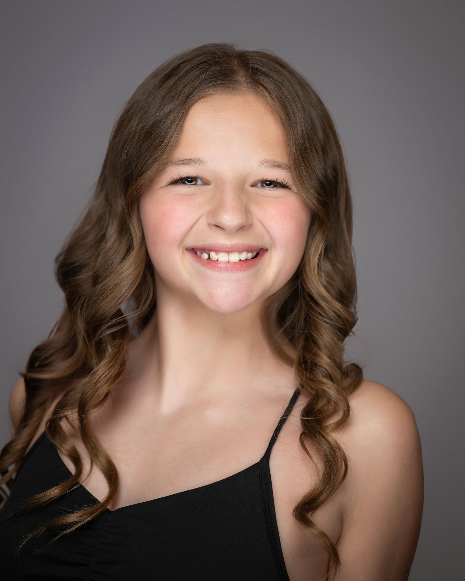 Professional portrait of young performer in black top with curled brown hair against gray background.
Pittsburgh Dance Photographer