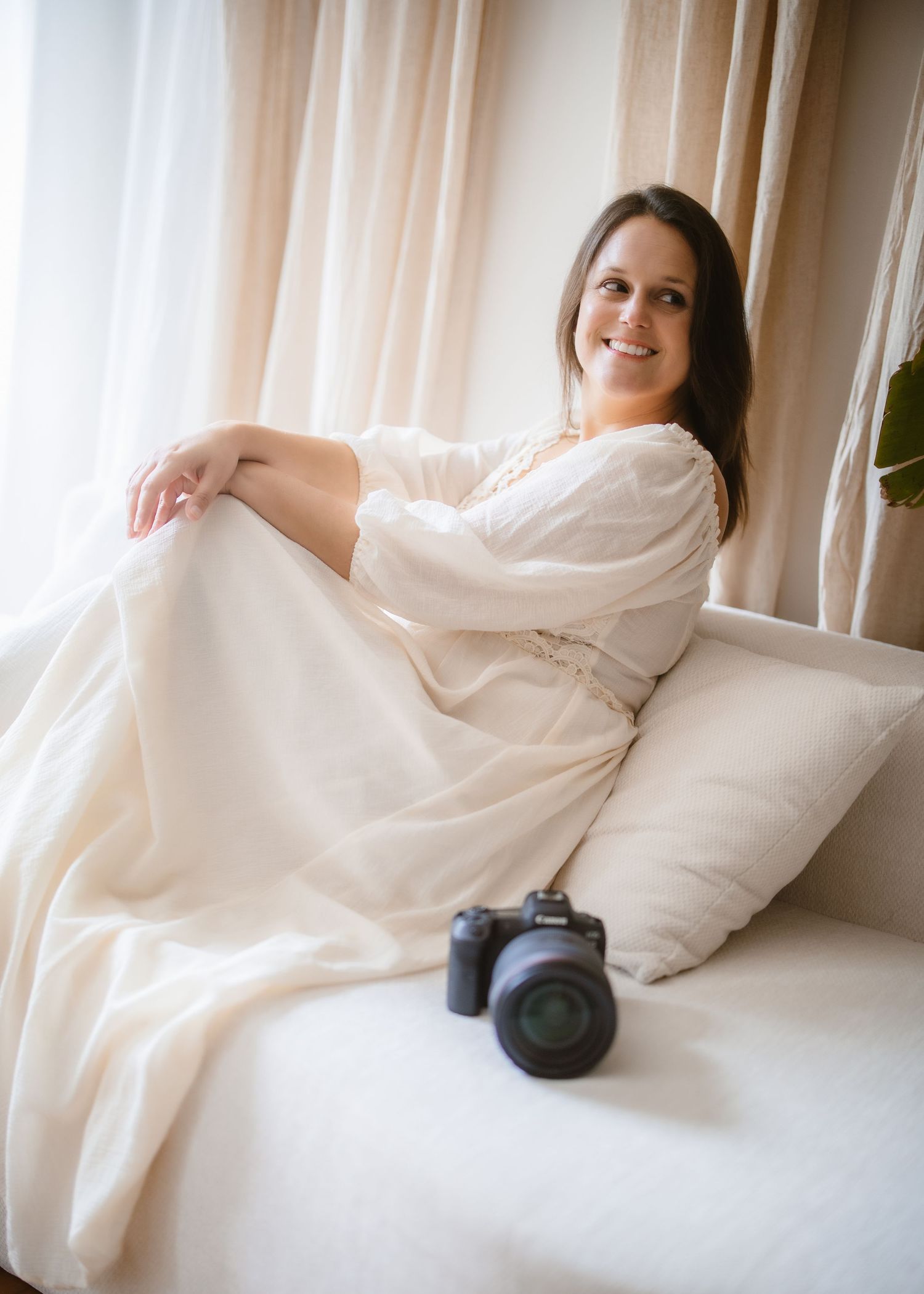 A photographer holds a vintage camera while posing in casual denim against a white wall.