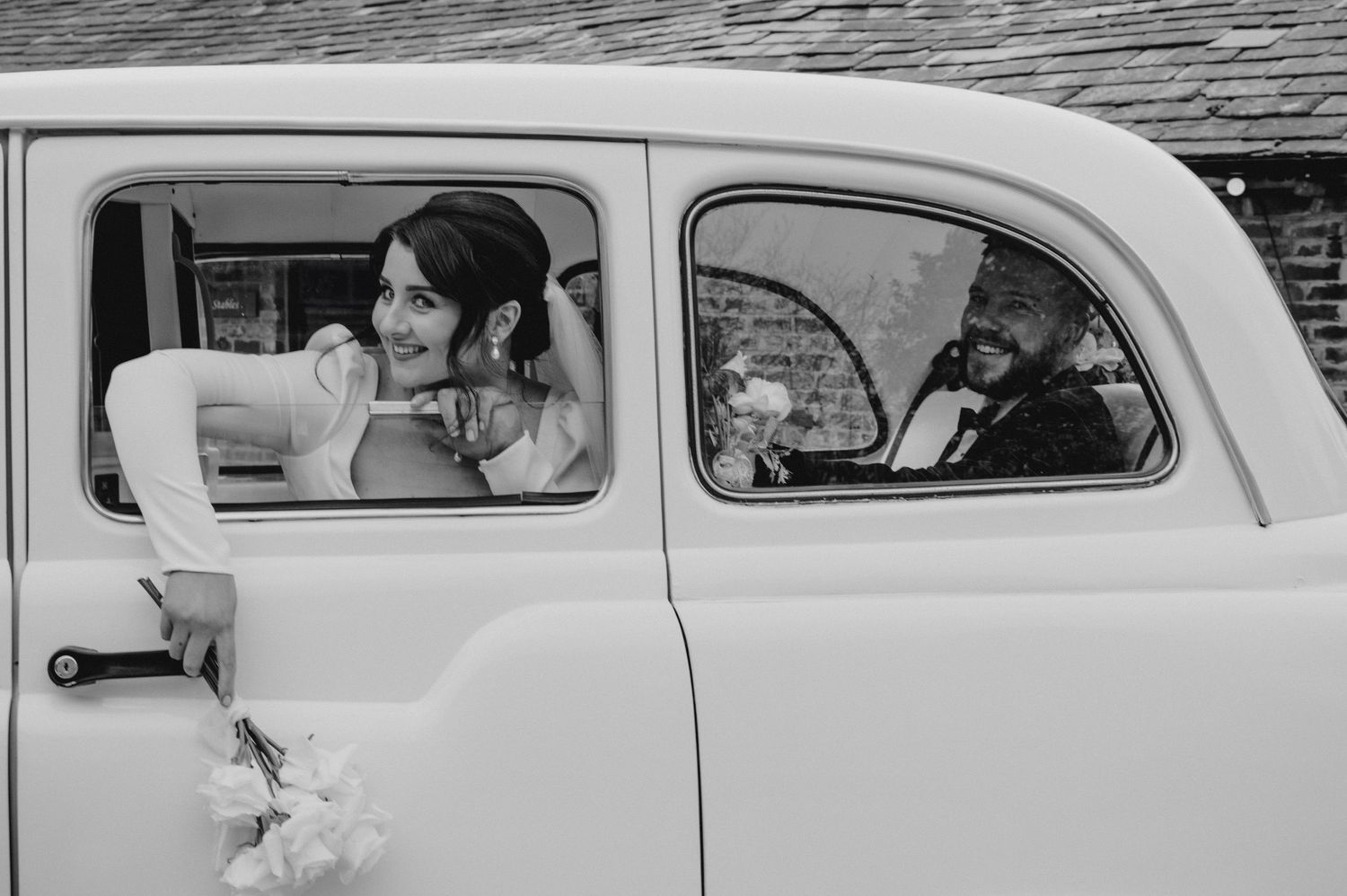 Classic vintage car captures a wedding moment in black and white photography.